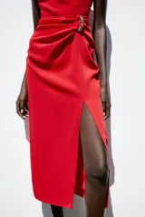 Vestido midi rojo de cuello redondo y sin mangas, con detalle de pliegues y fornitura en la cintura, y abertura frontal en el bajo.