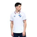 Remera tipo polo blanca de manga corta, con cuello y ribetes en las mangas con franjas azul marino, rojo y blanco. Lleva el logo Umbro bordado y el escudo del Club Nacional de Football estampado en el pecho.