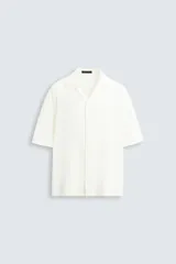 Camisa de hombre de corte relajado (relaxed fit), color blanco, con cuello bowling y manga corta. Presenta un tejido con estructura vertical y efecto lavado, con cierre frontal de botones al tono.