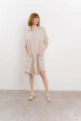 Vestido camisero corto color verde oliva, confeccionado en lino 100%. Tiene botones en la parte delantera, cuello camisero, mangas cortas con botón para arremangar y bolsillos laterales.