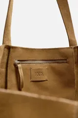 Bolso tipo shopper color marrón claro, fabricado en piel serraje. Cuenta con dos asas de mano y un bolsillo interior con cierre de cremallera.