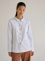 Camisa celeste de algodón con cuello clásico, cierre frontal con botones y mangas largas. Presenta volados en el frente y corte evasé.