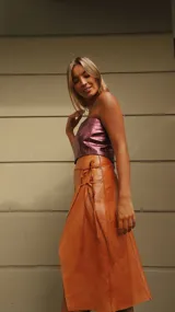 Falda midi de cuero color marrón, de corte recto y estilo portafolio. Se ata en los costados con tiritas.