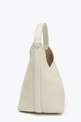 Bolso tipo saca de piel color blanco hueso con efecto granulado. Tiene asa de hombro y cierre con imán. Incluye cartera con bolsillo extraíble.