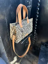 Cartera bandolera pequeña de cuero con estampado animal print, forro de tela y correa larga de cuero marrón.
