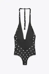 Bañador negro con estampado de lunares blancos, copas extraíbles, cuello halter con lazada y escote pico pronunciado. Detalle de flor en relieve en el pecho.