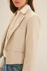 Saco corto color beige confeccionado en lino, con forro de poliéster y viscosa. Presenta solapas de muesca, cierre con un botón y corte cropped.