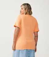 Remera color durazno de algodón con cuello redondo y mangas cortas. Presenta un estampado de piña con detalles de lentejuelas y la frase "Calor de Verão".