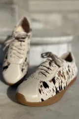 Zapatillas bajas con estampado animal print en blanco, marrón y negro, con puntera y talón en cuero color crema y suela de goma color caramelo.