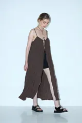Vestido largo marrón oscuro, con tirantes finos y escote pronunciado que se ajusta con cordones en el centro. El tejido es arrugado o plisado.