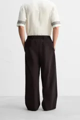 Pantalón relaxed fit color marrón oscuro confeccionado en tejido con mezcla de algodón y lino. Cintura elástica, bolsillos laterales y bolsillo trasero de plastrón. Perneras con pliegues frontales. Cierre en delantero con cremallera y botón.