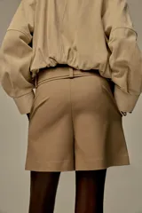 Shorts color marrón confeccionados en hilatura con algodón. Tiro alto y cintura doble con trabillas, bolsillos laterales y falso bolsillo con solapa en delantero. Detalle de costuras a contraste y cierre frontal con cremallera y ganchos metálicos.