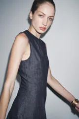 Vestido midi de denim azul oscuro, con cuello redondo y sin mangas. Corte entallado en la cintura y falda evasé. Cierre trasero con cremallera oculta.