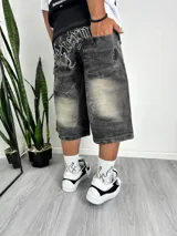 Bermuda de jean color negro gastado, tiro bajo y corte ancho (baggy), con bordado blanco en la parte trasera del bolsillo.