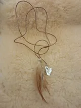 Gargantilla de cuero color beige con dije de pluma marrón y blanca y dije de cristal transparente.