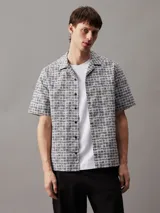 Camisa de manga corta con cuello cubano y corte boxy. Diseño con estampado de rejilla en blanco y negro y logo de Calvin Klein estampado.