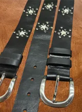 Cinturón de cuero negro con hebilla metálica plateada y apliques de estrellas de cuero con pelo natural y tachas metálicas.
