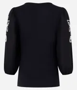 Blusa negra de rib con escote cuadrado, mangas largas abullonadas y bordado floral blanco en los laterales de las mangas.