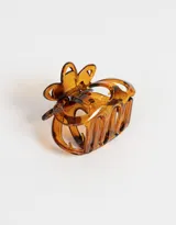 Broche para el pelo color carey con forma de pinza y detalle de flor con tres pétalos calados a cada lado.
