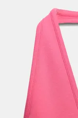 Top de color fucsia con escote pronunciado en V y cuello halter. Presenta una costura horizontal que marca la transición entre el busto y el torso.