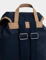 Mochila azul marino con detalles en cuero sintético color camel. Tiene solapa superior con cierre de hebilla, doble bolsillo frontal con hebilla, correa de ajuste y manija superior.