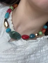 Collar corto de cuentas de colores y formas variadas, con detalles dorados. Las cuentas incluyen tonos como verde, rojo, turquesa, naranja y dorado.