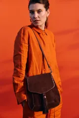 Bandolera de cuero gamuza color chocolate, con correa larga regulable, solapa con detalle de pespuntes y borla decorativa.