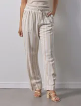 Pantalón de lino a rayas verticales color beige y blanco, con pretina ancha elastizada, lazo de ajuste y bolsillos inclinados.