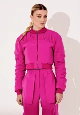 Campera bomber fucsia de cupro con forro y acabados acolchados. Tiene largo corto, cuello, puños y bajo rectos, mangas con detalles acolchados y pliegues, y cierre frontal con cremallera metálica.