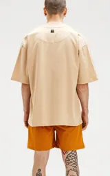 Remera color beige de corte crop y calce oversize, con hombros caídos y cuello redondo.