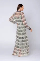 Vestido largo camisero de tejido de punto con estampado zigzag en tonos tierra, verde claro y blanco. Presenta cuello en V con solapas oscuras, cierre frontal de botones y mangas largas abullonadas con puños oscuros. Se ajusta a la cintura con un lazo ancho de satén oscuro.