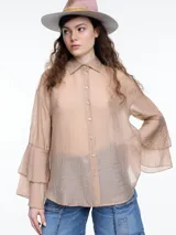 Camisa color beige traslúcido, de corte holgado, con cuello clásico, cierre frontal con botones y mangas largas con volados.