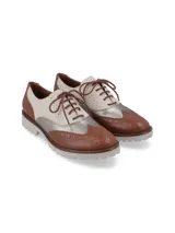 Zapato Oxford de cuero color cognac, blanco y plateado, con cordones marrones, detalles de perforaciones y suela de goma blanca.
