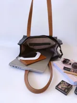 Bolso tipo tote bag de cuero negro con forro de tela, doble asa de cuero color suela, bolsillo frontal y bolsillo interno.