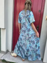 Vestido largo de seda con estampado floral en tonos turquesa, azul y blanco. Tiene escote en V y mangas cortas.