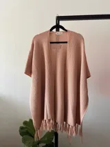 Ruana rosa pastel tejida en acrílico con flecos.