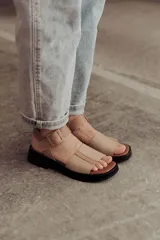 Sandalias bajas color arena, con tiras anchas de cuero y hebilla lateral.