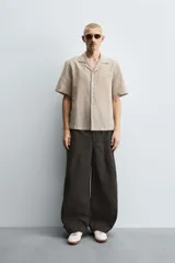 Pantalón cargo de corte ancho y relajado, color verde oscuro o negro, con cintura elástica, bolsillos laterales de parche y bolsillos traseros de vivo. Presenta pliegues verticales marcados en la parte delantera y cordones ajustables en los bajos.