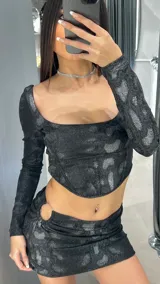 Conjunto negro brillante con estampado animal print, compuesto por un top de mangas largas con escote cuadrado y una minifalda con detalle de aro metálico en la cadera.