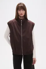 Chaleco marrón oscuro con cuello alto, cierre frontal de cremallera plateada y puños y bajo elásticos.