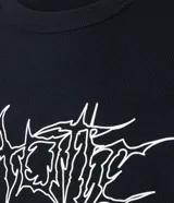 Remera negra de algodón con textura y corte oversized. Presenta estampa frontal con lettering gótico, siglas 'NY' dentro de un círculo y coordenadas geográficas.