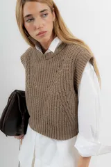 Chaleco de lana color crema, tejido a punto perlado con calado en la parte delantera. Tiene cuello a la base y silueta cuadrada.