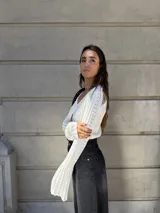 Saco corto de tejido de punto color blanco, con mangas largas y anchas con volados en los puños, y cierre frontal con botones.