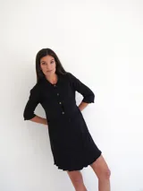 Vestido corto verde oscuro de tejido de punto acanalado, con cuello camisero, cierre frontal con botones, mangas 3/4 y bolsillos de parche.