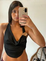 Top negro con escote drapeado, espalda descubierta y detalle de broche dorado en el hombro.