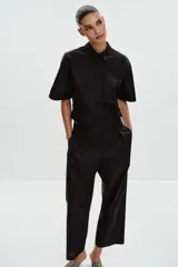 Camisa negra de popelín con cuello solapa y manga ancha por debajo del codo. Detalle de pinzas en la espalda y cierre frontal con botones ocultos por solapa.