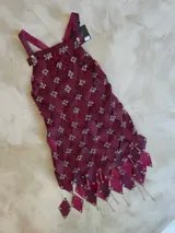 Vestido corto de diseño exclusivo, color bordó, confeccionado artesanalmente con piezas de material texturado (efecto cocodrilo) unidas con argollas metálicas. Presenta tirantes ajustables y un ruedo con terminaciones en forma de rombos colgantes con detalles metálicos.