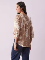 Blusa de crepe color beige con estampado de hojas blancas, cuello redondo con escote en V y lazo de ajuste, mangas 3/4 con tajo.