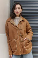Campera marrón con interior de corderito y exterior de eco cuero, con cierre frontal con alamares metálicos.