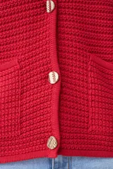 Chaqueta tejida roja con botones metálicos dorados y cuello redondo.